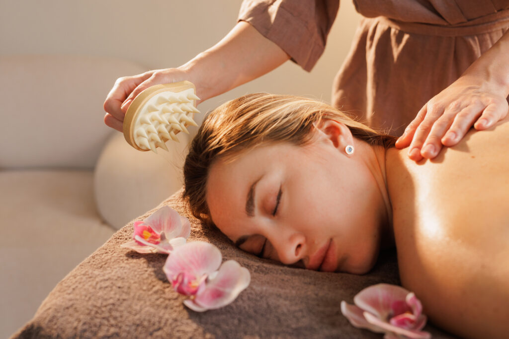 therapist uses a spiked massage tool to gently stimulate the woman's scalp during a calming spa session, enhancing circulation, relaxation, and stress relief in a tranquil setting.
